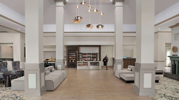 A spacious lobby with a central seating area, a reception desk, and a display of amenities.