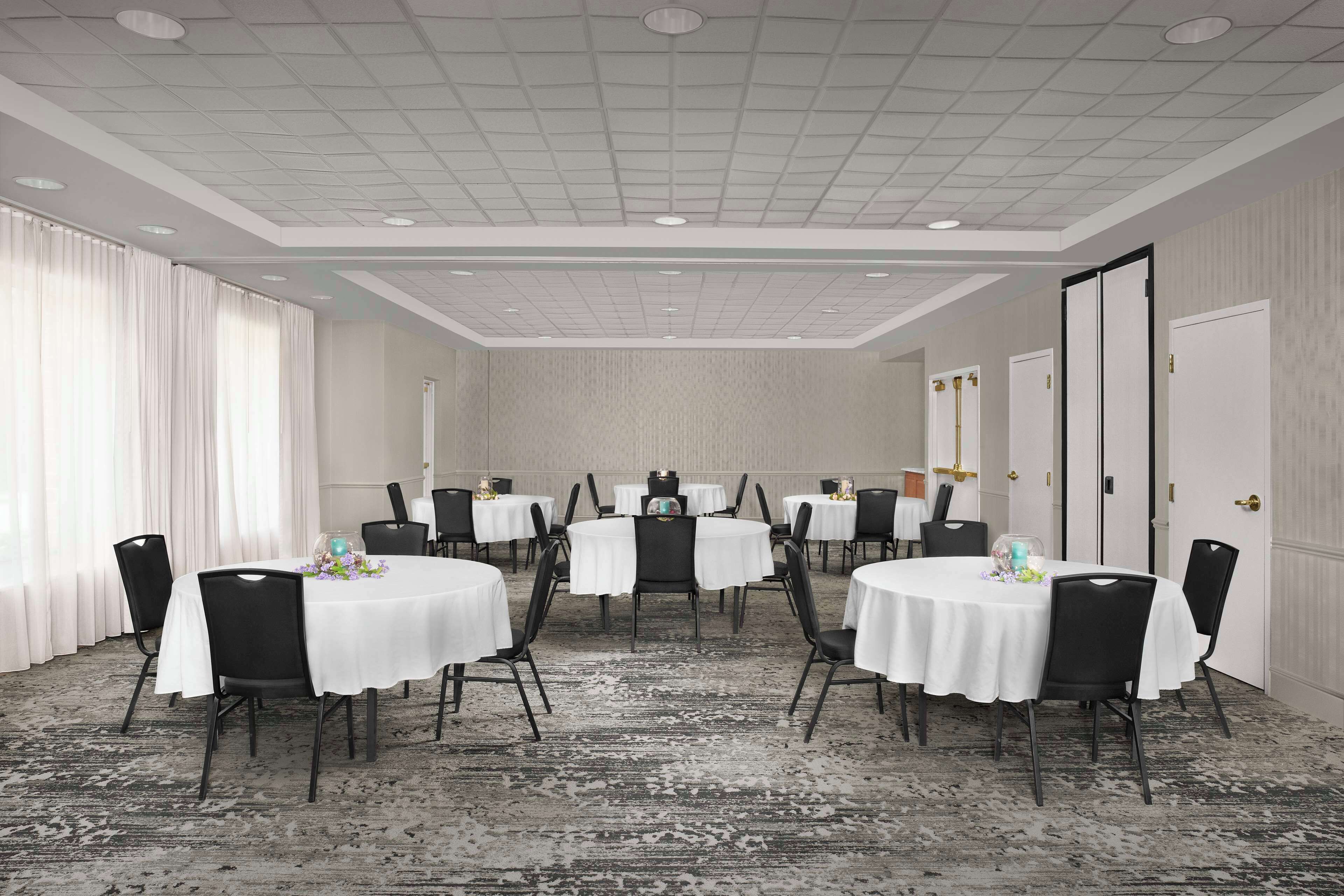 A conference room with multiple round tables, black chairs, and white tablecloths.