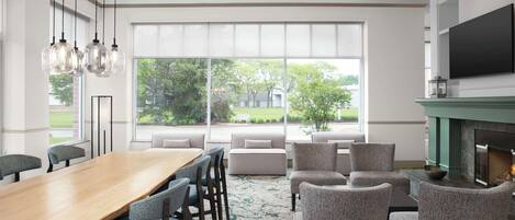A modern dining area with a wooden table and chairs, a fireplace, and large windows offering a view of the outdoors.