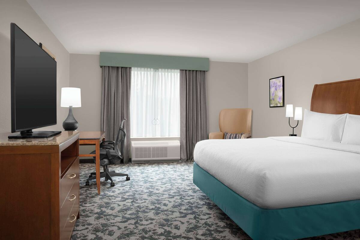A hotel room with a large bed, a desk with a computer, a chair, and a television.