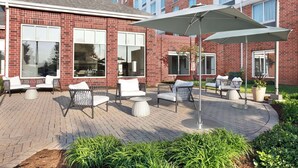A brick building with large windows and a patio area with outdoor furniture and a large umbrella.