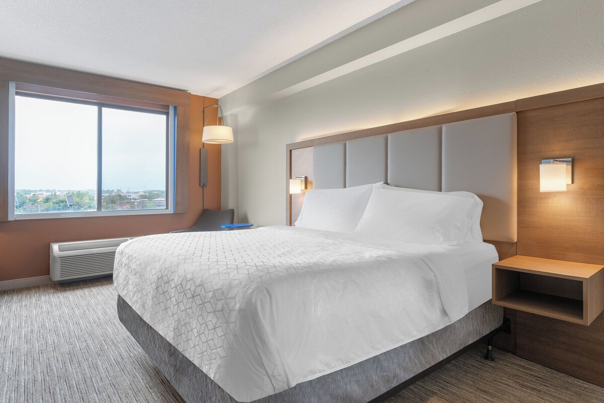Een hotelkamer met een groot bed, een nachtkastje, een raam en een wandlamp.