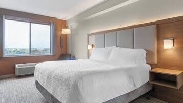 Habitación de hotel con una cama grande, una mesita de noche, una lámpara de pared y una ventana.