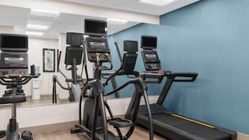 Un gimnasio con equipo de ejercicio, incluyendo cintas de correr y elípticas, y un espejo grande.