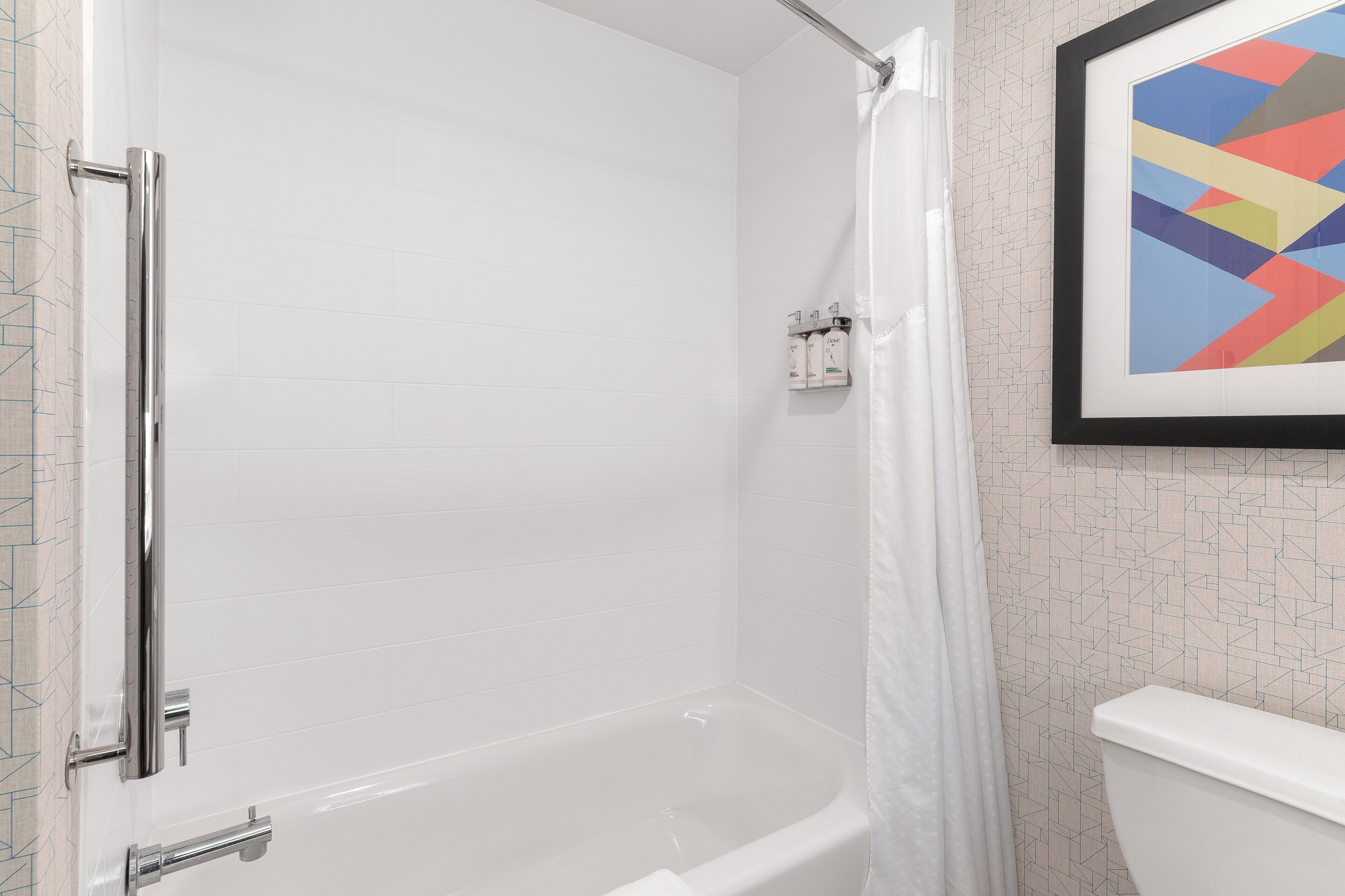 Une salle de bain avec une baignoire blanche, un rideau de douche, des toilettes et un tableau abstrait encadré accroché au mur.