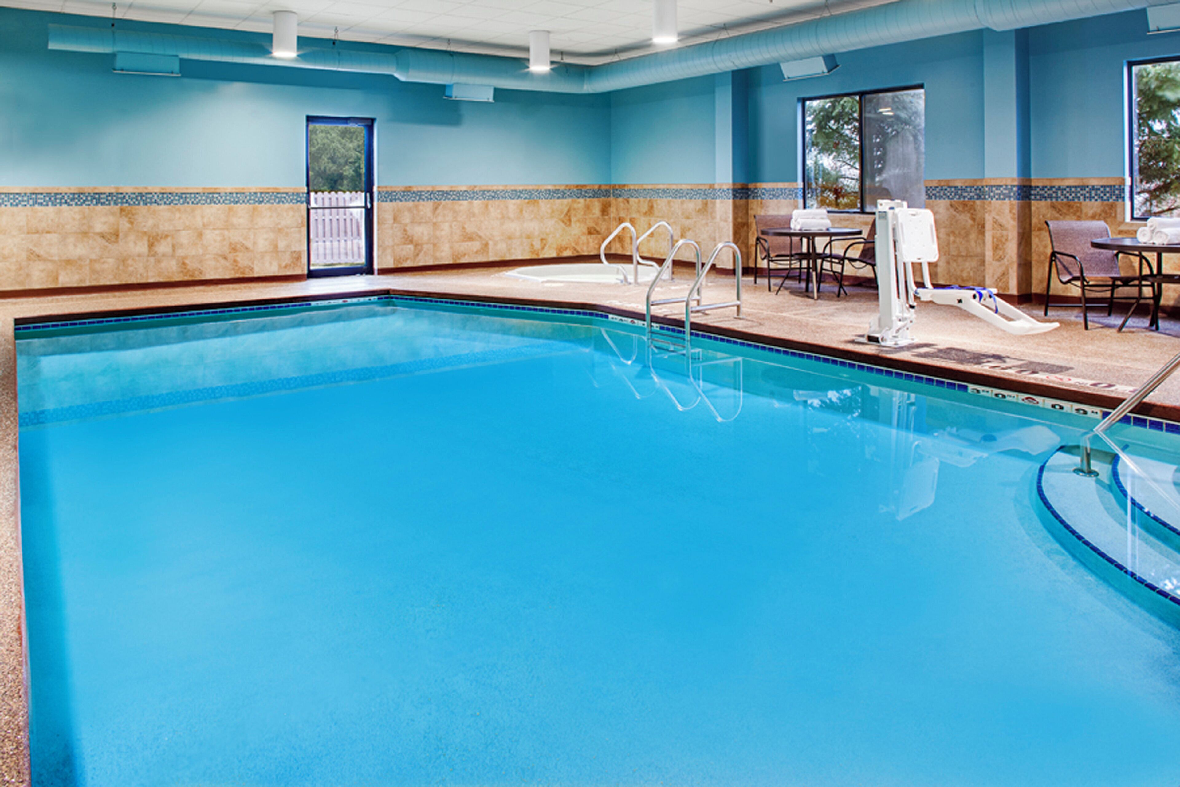 A swimming pool with a clear blue water, a pool ladder, and a seating area with tables and chairs.