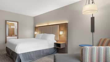 A hotel room with a large bed, bedside tables, a mirror, a hanging lamp, and a patterned chair.