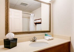Un baño de hotel con lavamanos, espejo, toallero y caja de pañuelos.