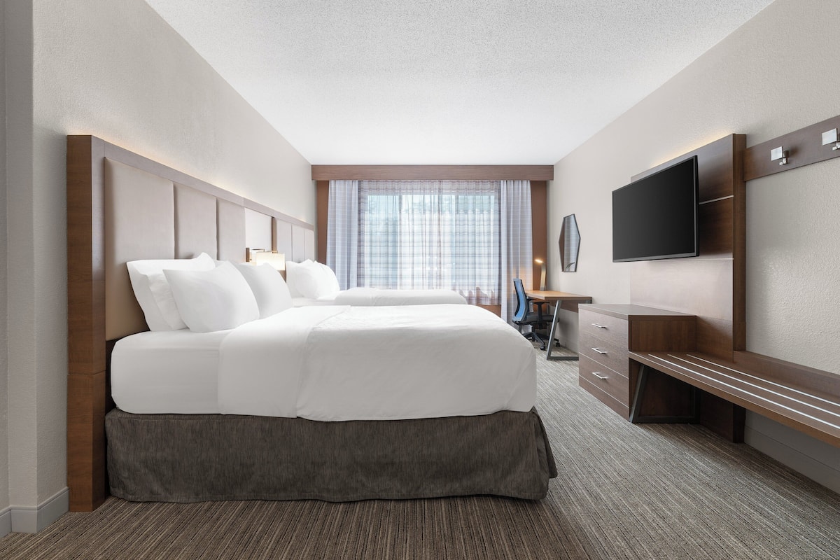 Ein Hotelzimmer mit einem großen Bett, einem Schreibtisch, einem Flachbildfernseher und einem Fenster mit Vorhängen.