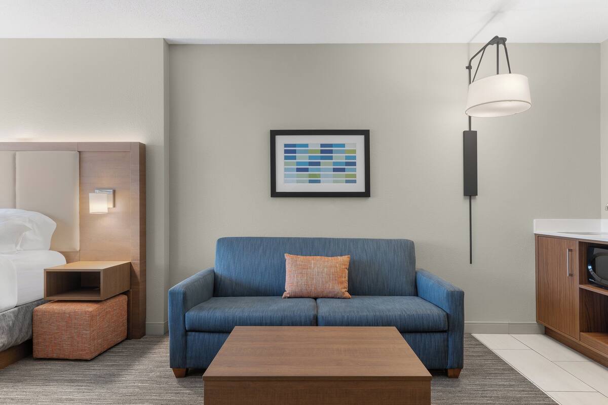 Ein modernes Hotelzimmer mit einem blauen Sofa, einem Holztisch, einem gerahmten Kunstwerk an der Wand und einem Nachttisch mit Lampe.
