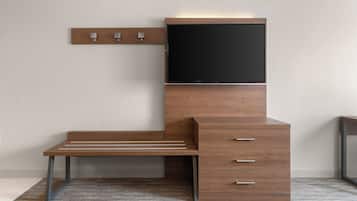 Una habitación moderna y compacta con un escritorio de madera, televisión integrada y un pequeño armario.