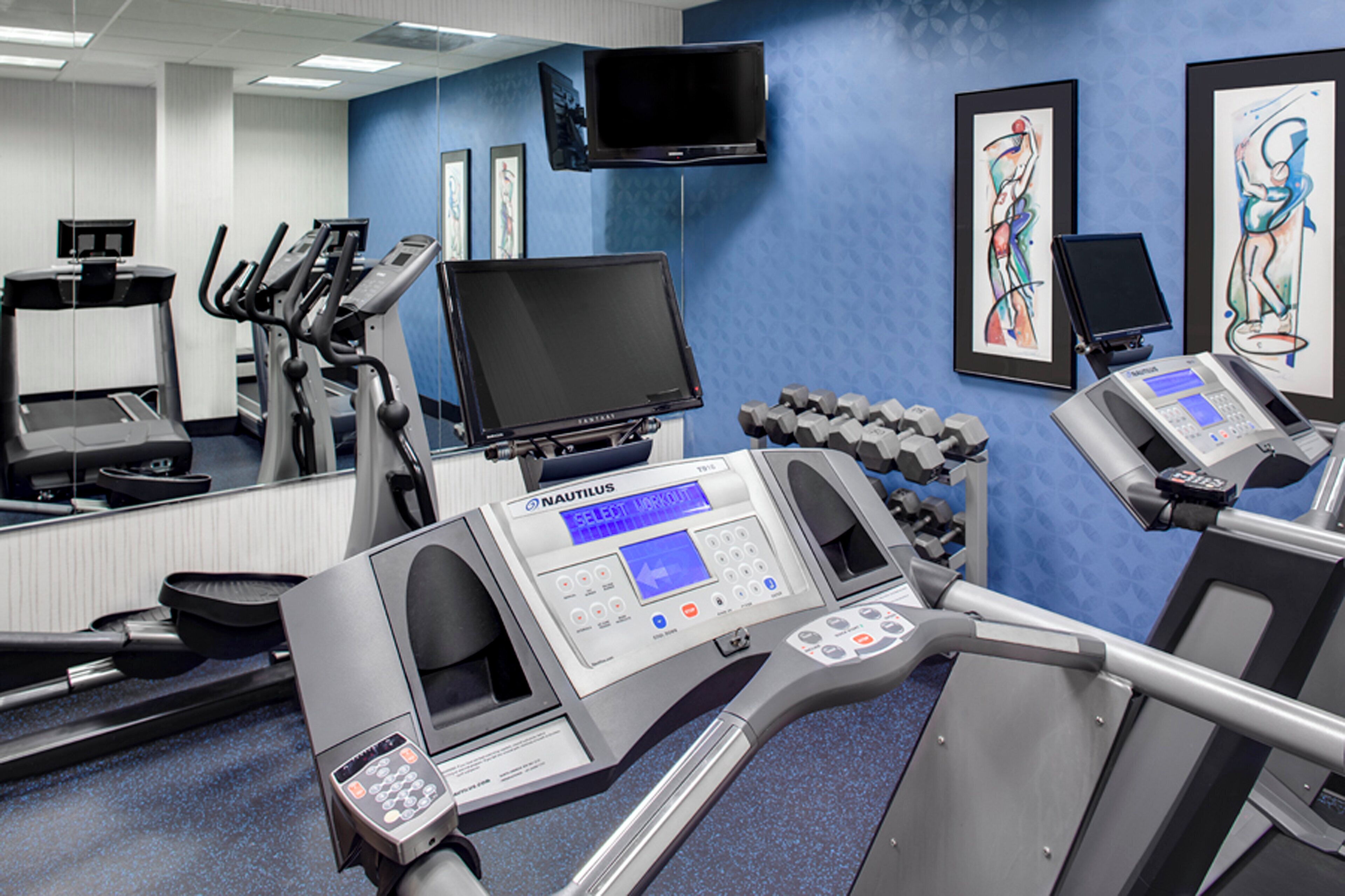 A gym with treadmills, a Nautilus exercise machine, dumbbells, and a television on the wall.