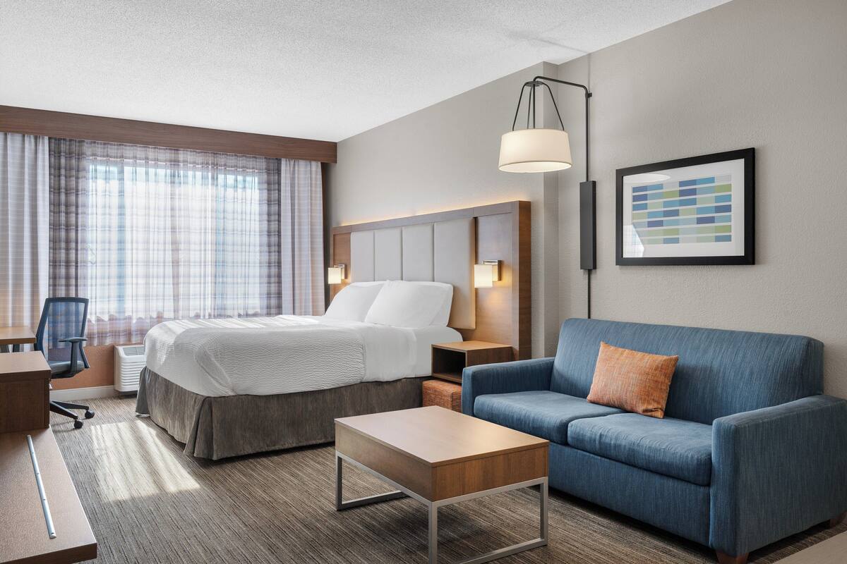 Ein Hotelzimmer mit einem Bett, einem blauen Sofa, einem Holztisch, einem Schreibtisch und einem Sessel.