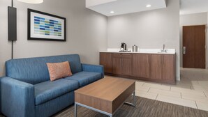 Een moderne woonkamer met een blauwe bank, een houten salontafel en een keuken met houten kastjes en een wit aanrecht.