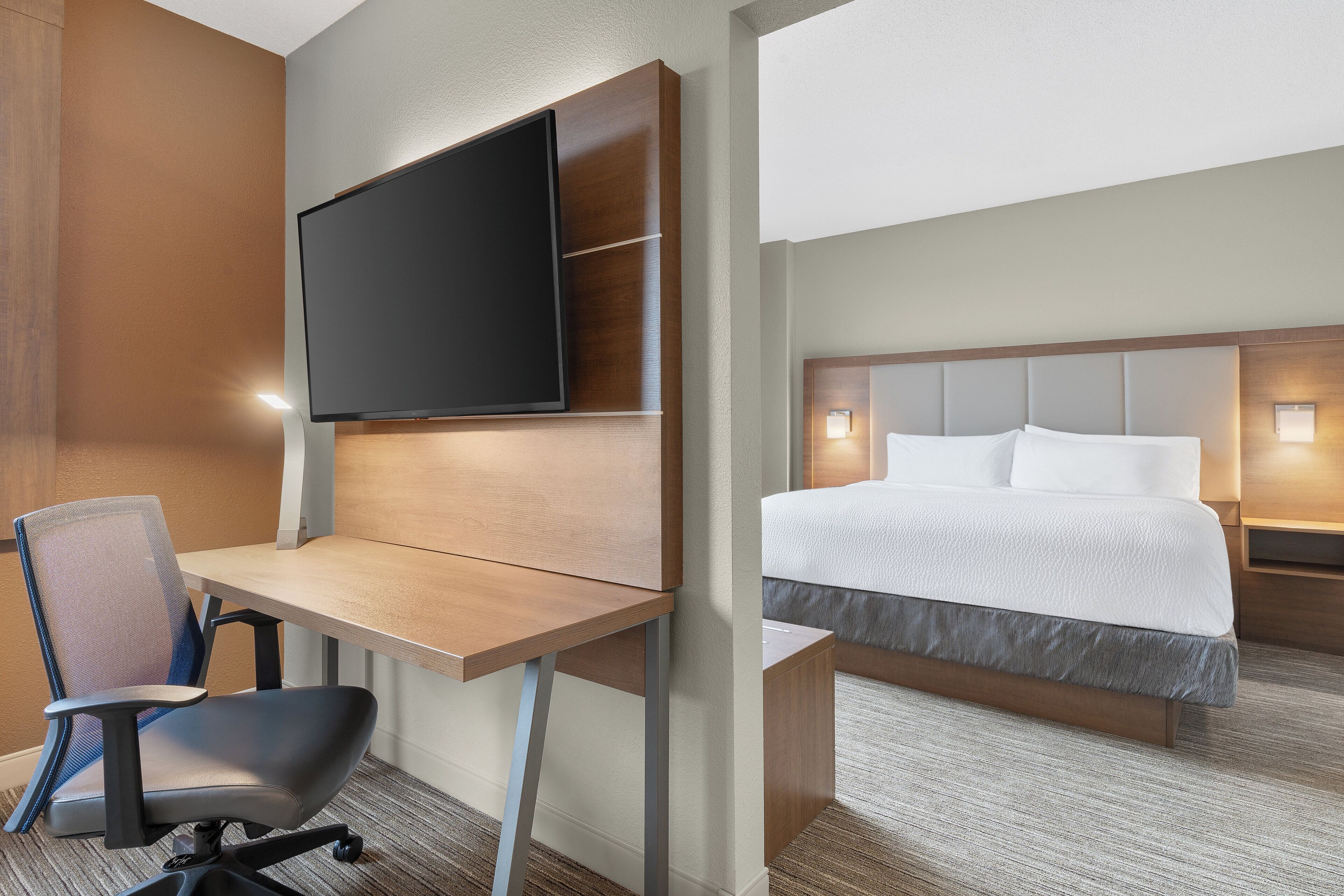 A hotel room with a desk, chair, flat-screen TV, and a bed with a headboard.