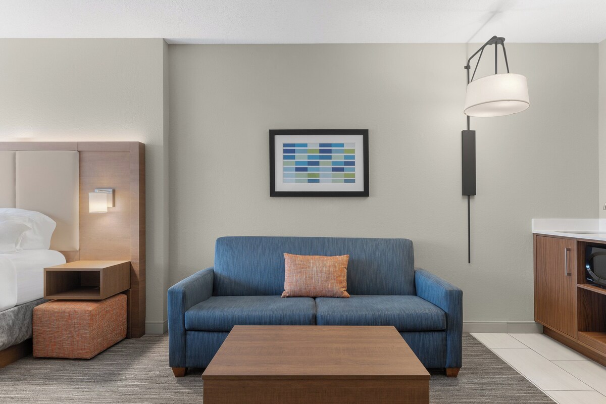 Ein modernes Hotelzimmer mit einem blauen Sofa, einem Holztisch, einem gerahmten Kunstwerk an der Wand und einem Nachttisch mit Lampe.