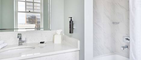 A modern bathroom with a marble sink, a large mirror, a shower with a rain showerhead, and a towel rack.