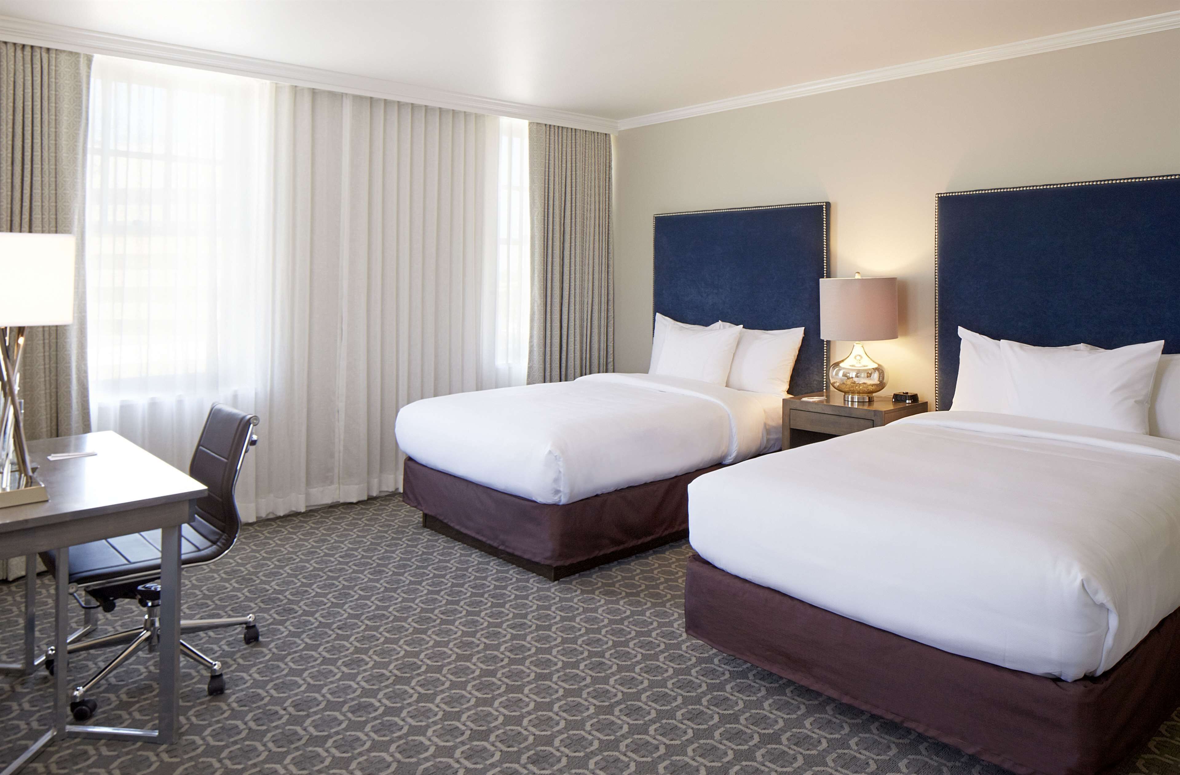 A hotel room with two beds, a desk, and a chair.