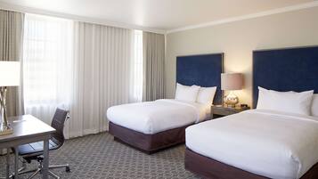 A hotel room with two beds, a desk, and a chair.