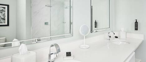 A modern bathroom with two sinks, a large mirror, and a glass-enclosed shower.