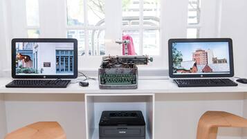 Two HP desktop computers with monitors displaying cityscapes, a Brother printer, and wooden chairs.