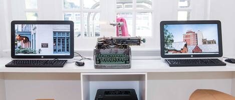 Dois computadores HP com monitores exibindo paisagens urbanas, uma impressora Brother e cadeiras de madeira.