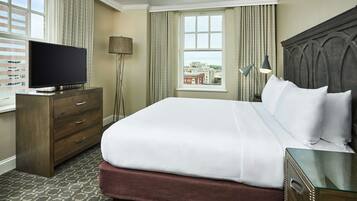 A hotel room with a large bed, a TV on a wooden dresser, a window with a city view, and a lamp.