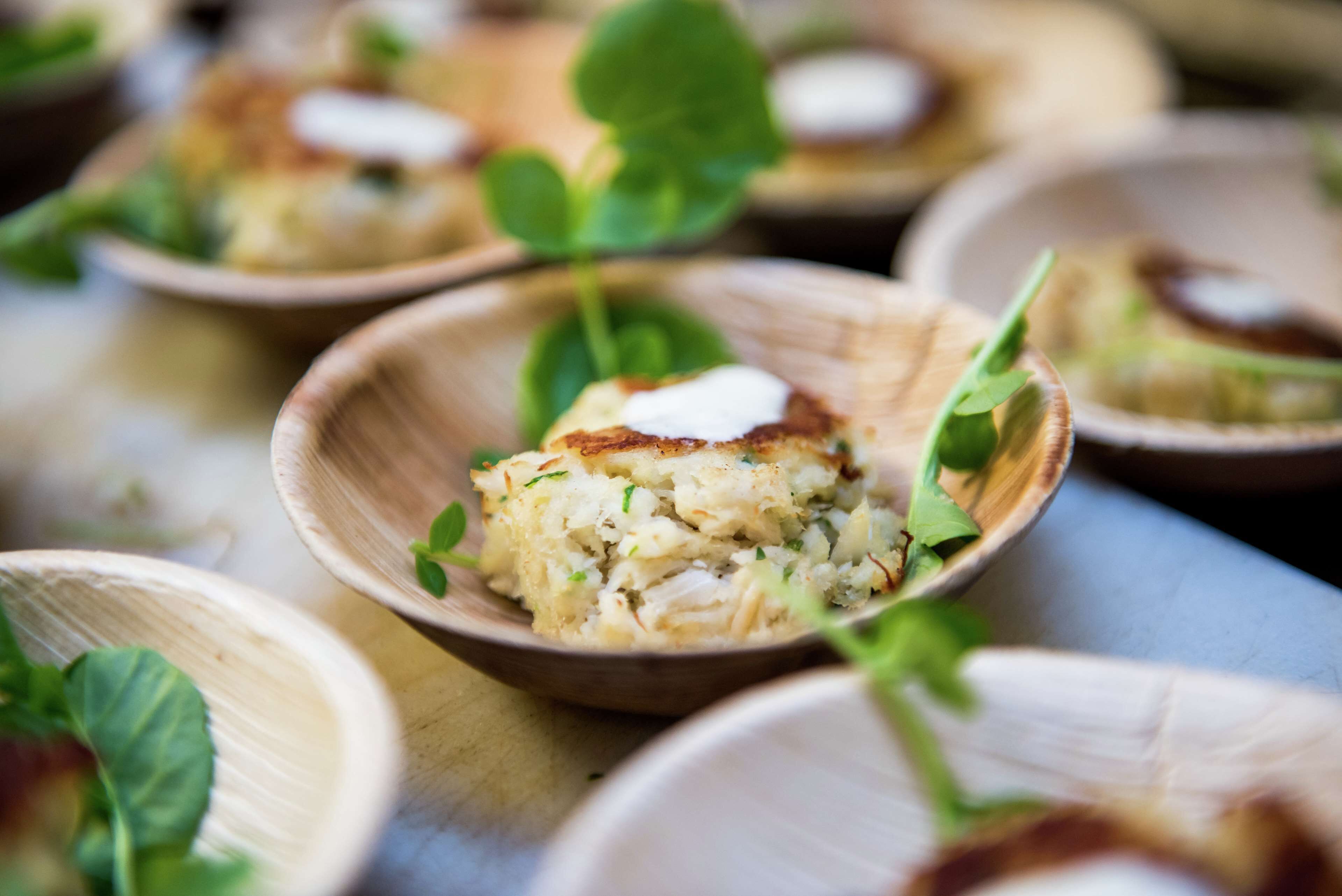 A close-up of a wooden bowl containing a food item, possibly a salad or appetizer, garnished with a leaf and a dollop of cream or sauce.