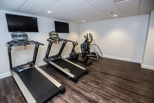 Un gimnasio con cintas de correr, bicicletas estáticas y una pantalla de televisión.