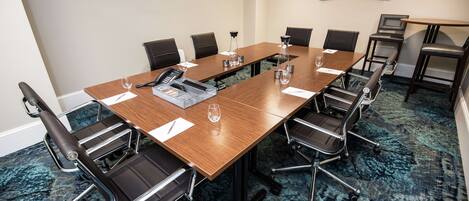A conference room with a long table, black chairs, a projector screen, and a carpeted floor.