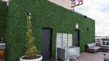 Eine Dachterrasse mit grüner Wand, einem Topfbaum, Sitzgelegenheiten im Freien und Blick auf die Stadt.
