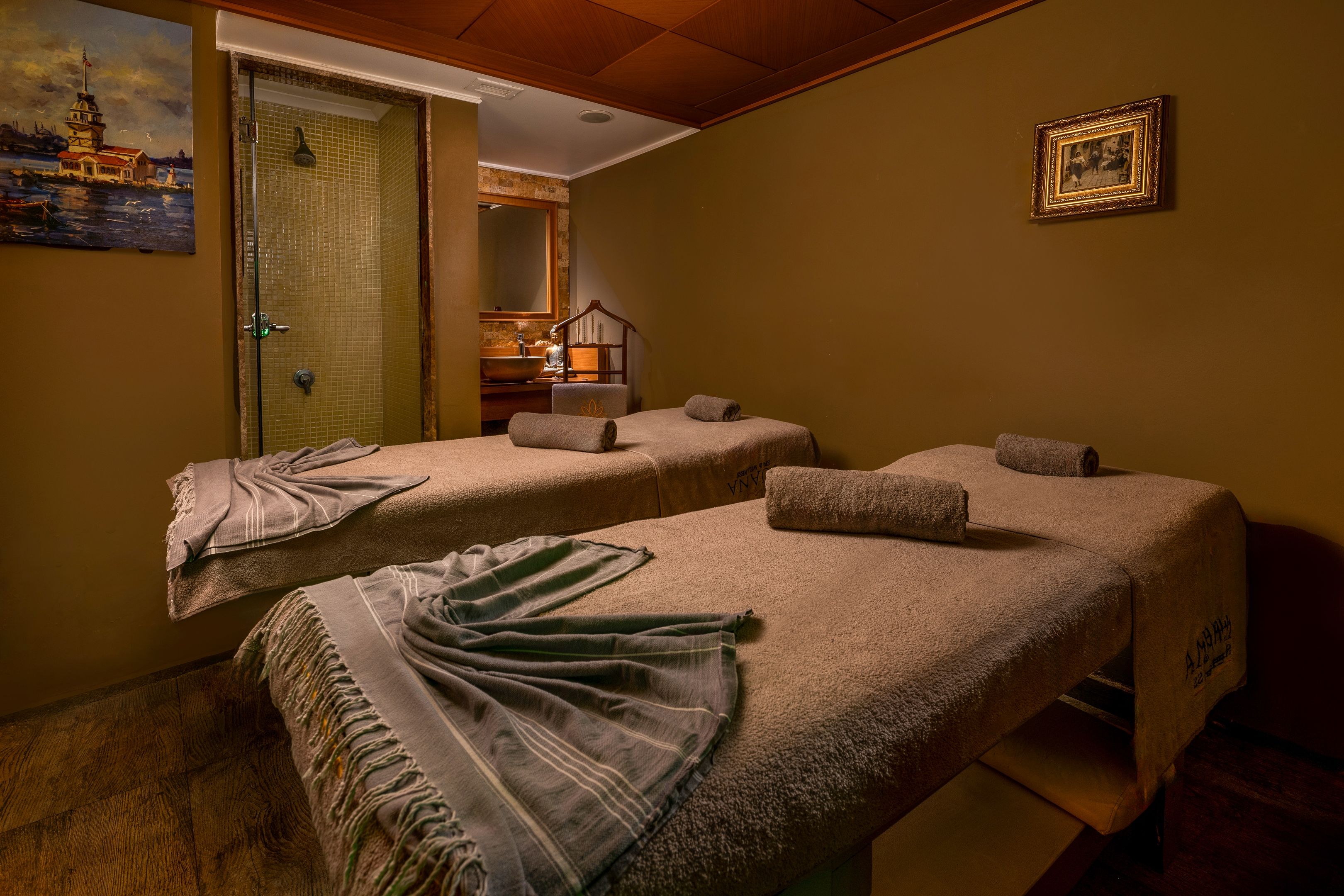 A room with two massage tables, a wooden ceiling, a painting, and a framed picture on the wall.