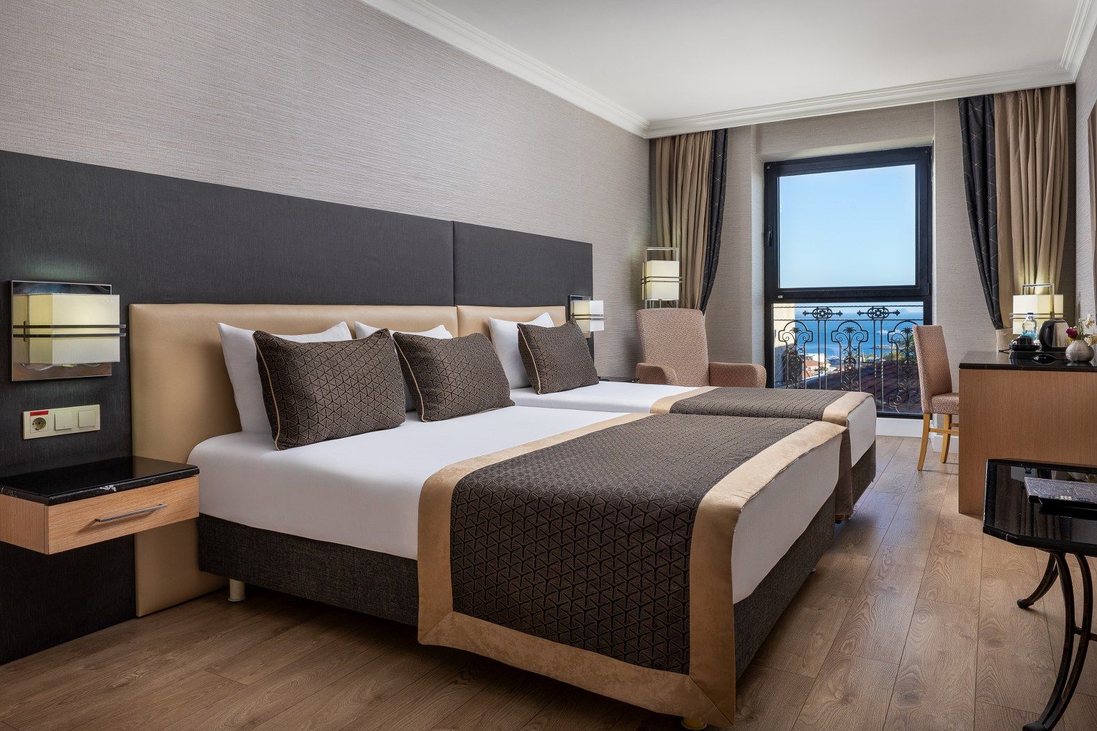 A hotel room with a large bed, bedside tables, a desk, and a view of the sea.