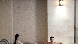 A couple relaxing in a hot tub with a tiled wall and a decorative light fixture in the background. - Darkhill Hotel (Istanbul)