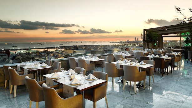 A rooftop restaurant with tables set for dining, overlooking a cityscape and the sea at sunset. - Darkhill Hotel (Istanbul)