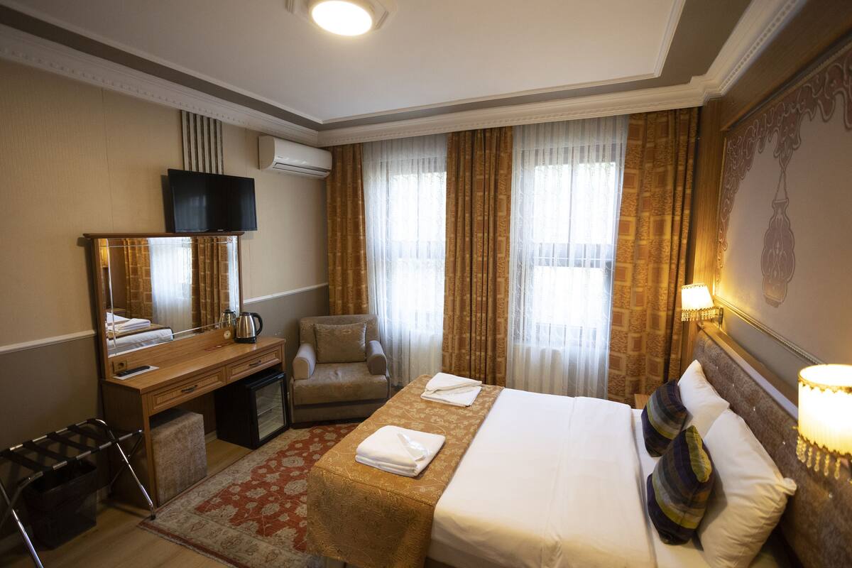 A hotel room with a bed, a desk, a chair, a TV, and a window with curtains.