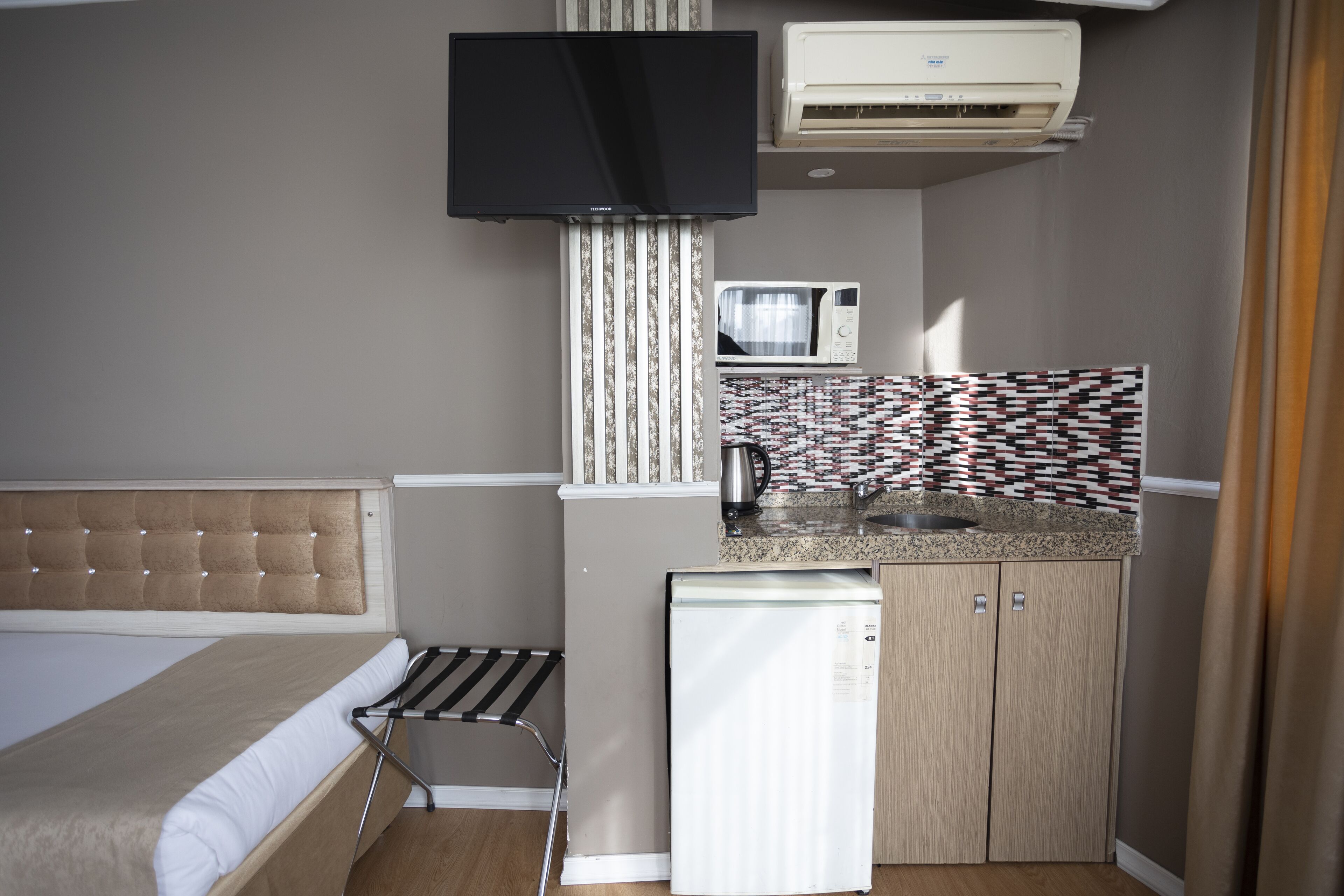 Una habitación de hotel compacta con cama, kitchenette pequeño, televisor y aire acondicionado.