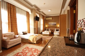 A hotel room with a sofa, two single beds, a small table with a kettle, and a TV mounted on the wall.