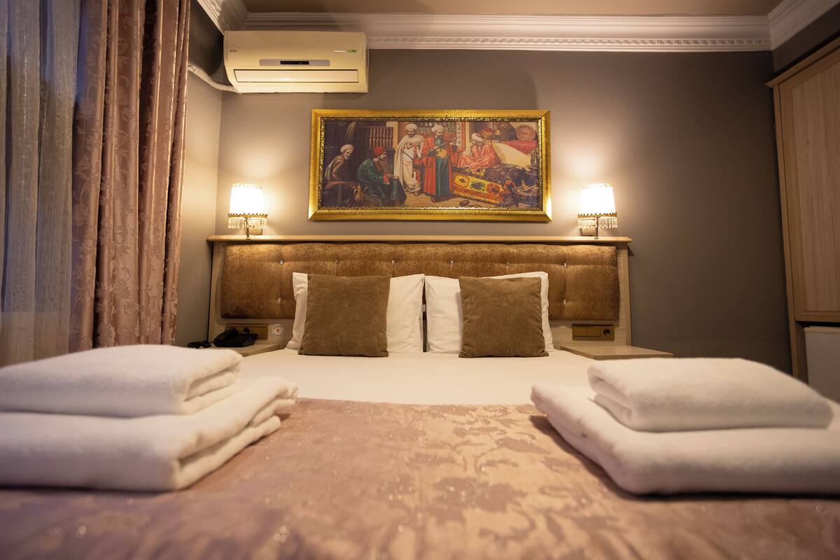 A hotel room with a bed, two bedside lamps, a painting on the wall, and a window with curtains.