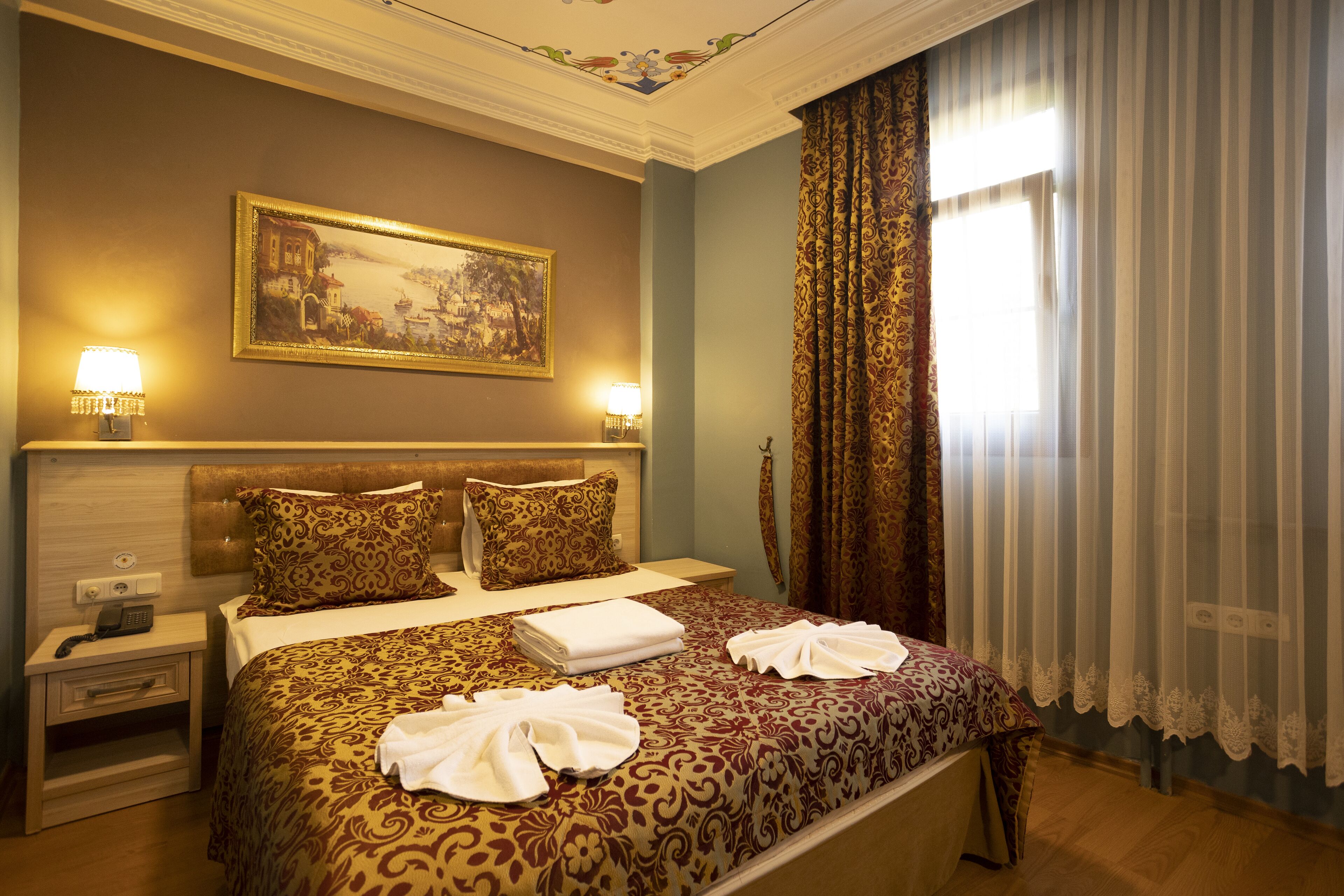 A hotel room with a large bed, two bedside lamps, a painting on the wall, and a window with curtains.