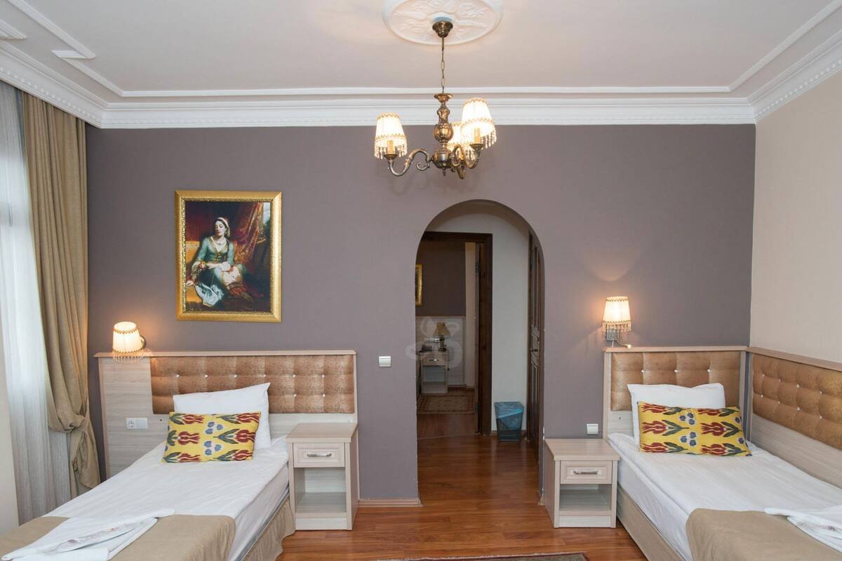 A hotel room with two beds, a chandelier, a painting, and a hallway leading to another room.