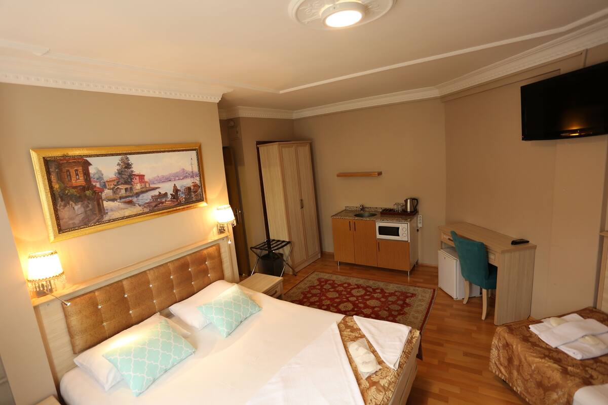 A hotel room with a large bed, a desk, a television, and a painting on the wall.