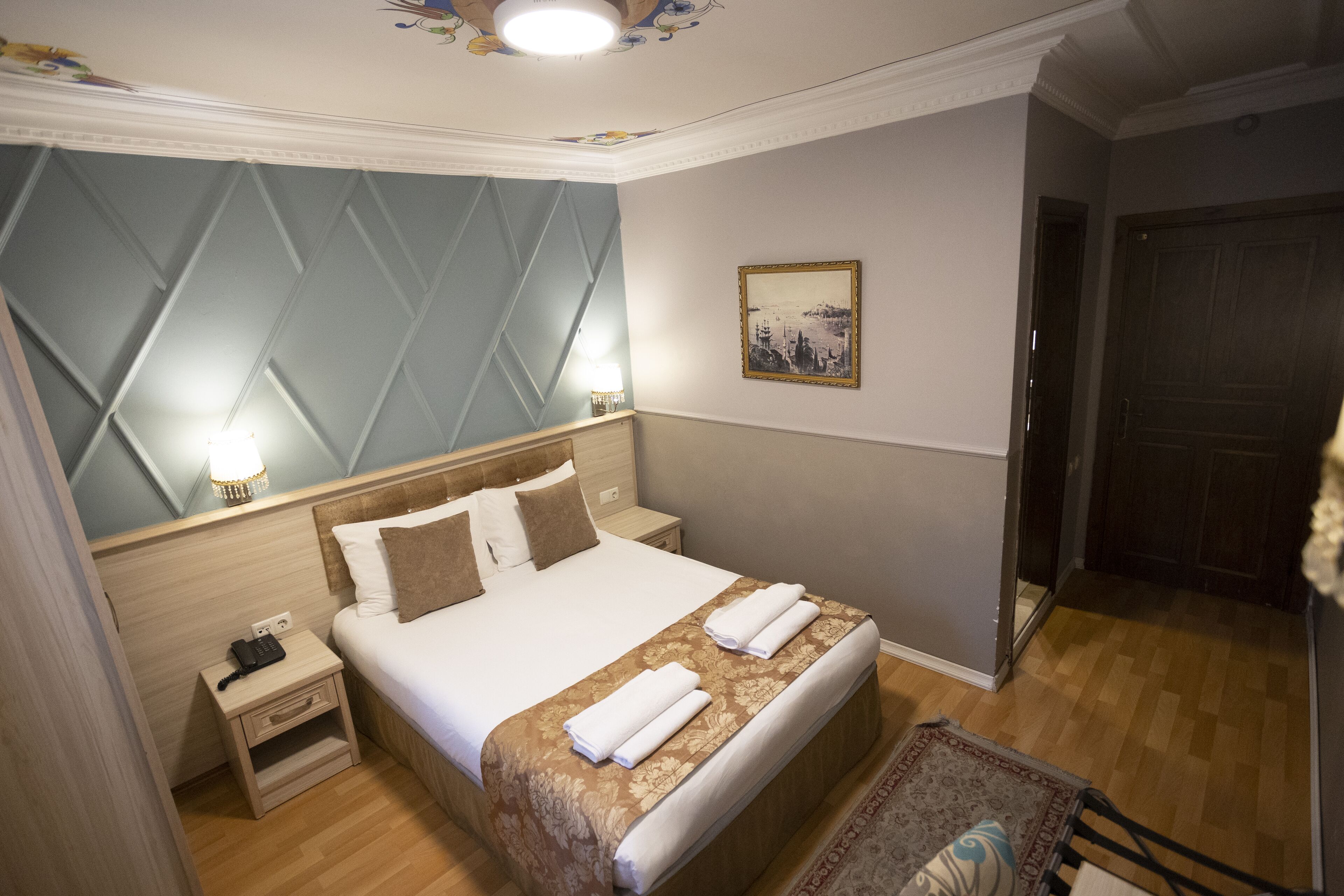 Una habitación de hotel con una cama grande, lámparas de noche, una mesita de noche, piso de madera y una puerta.