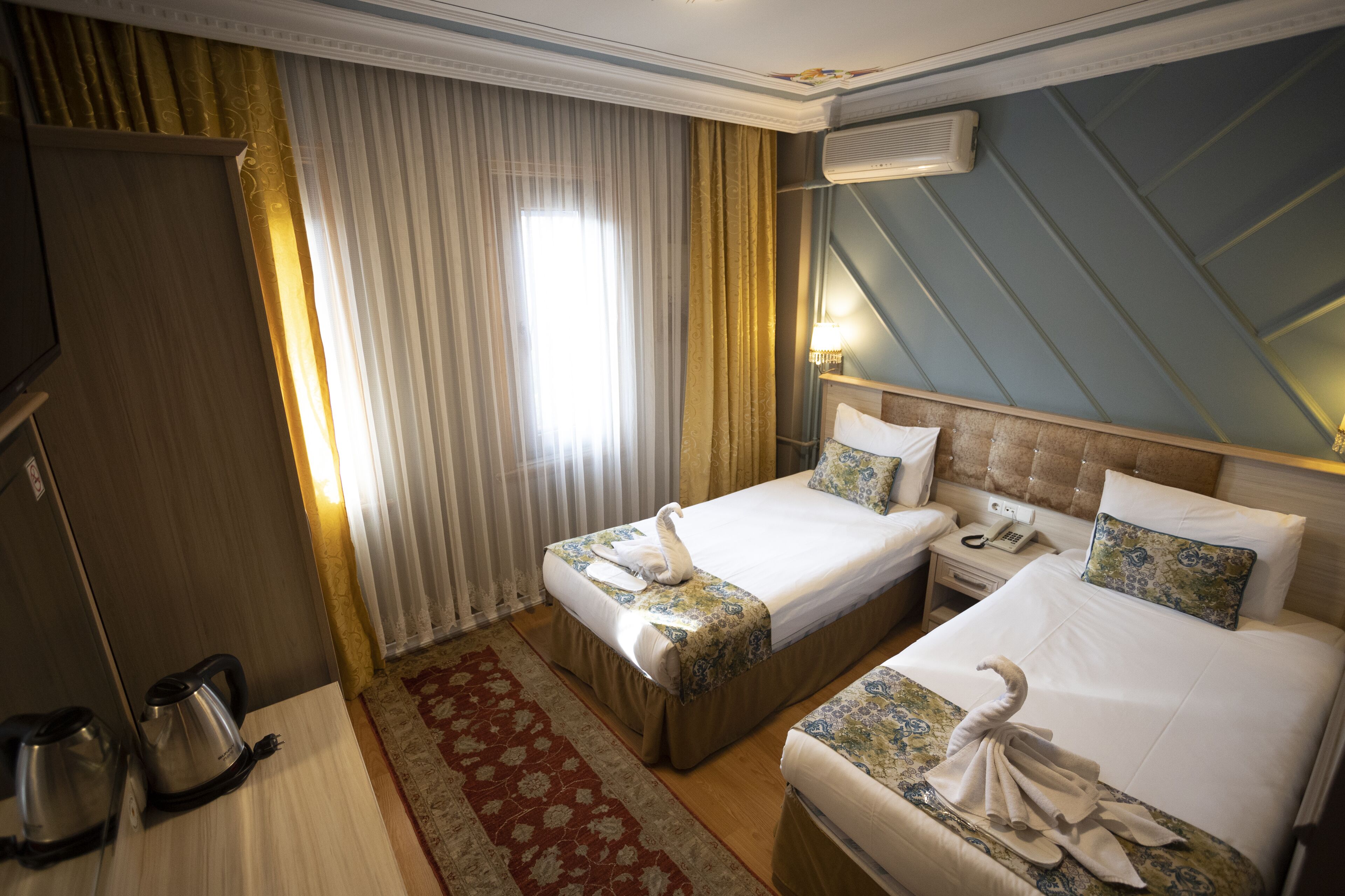 A hotel room with two beds, a minibar, a desk, and a window with curtains.