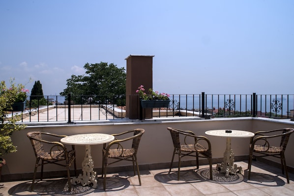 A balcony with wicker chairs and a round table, overlooking a scenic view.