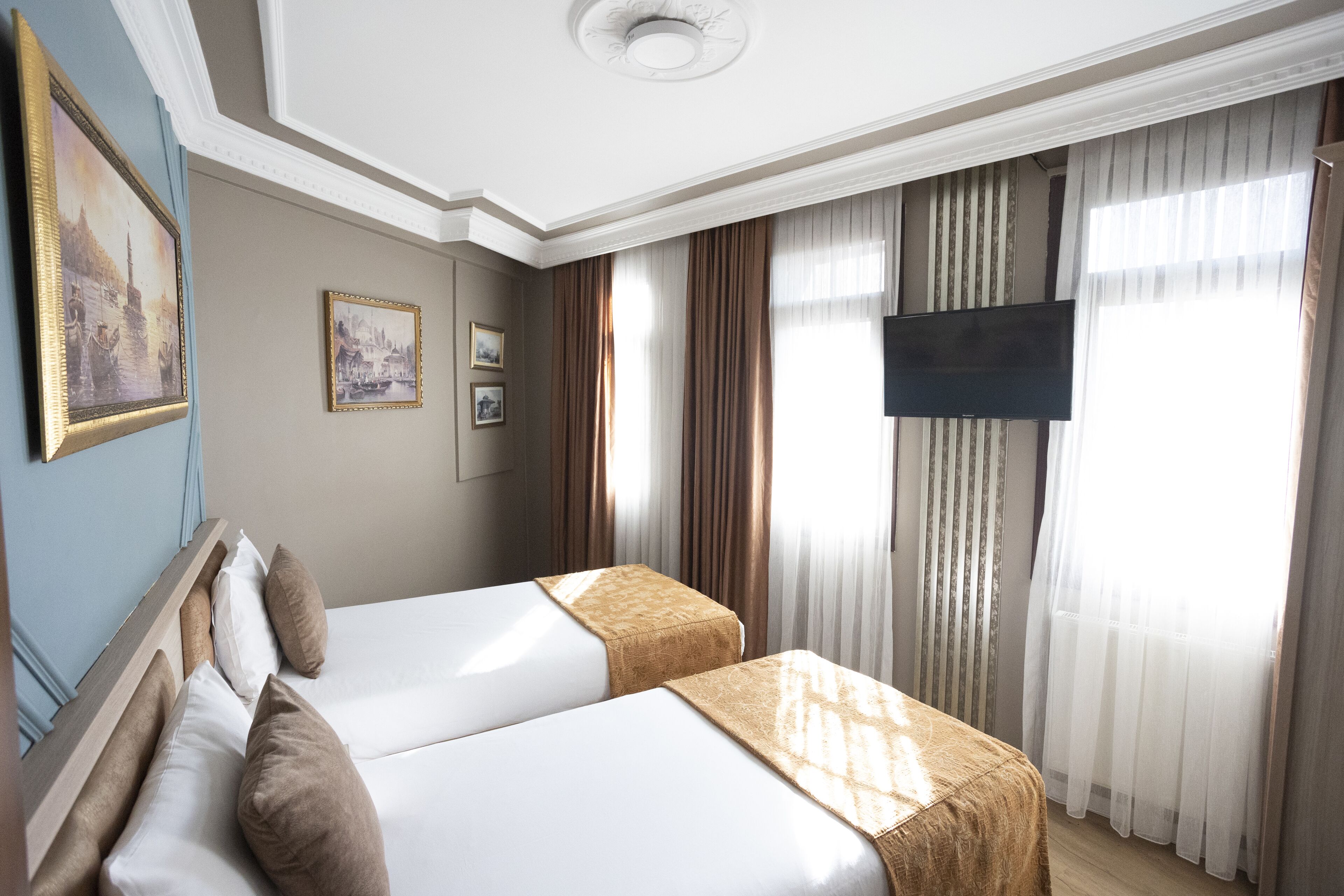 A hotel room with two beds, a flat-screen TV, and a large window with curtains.
