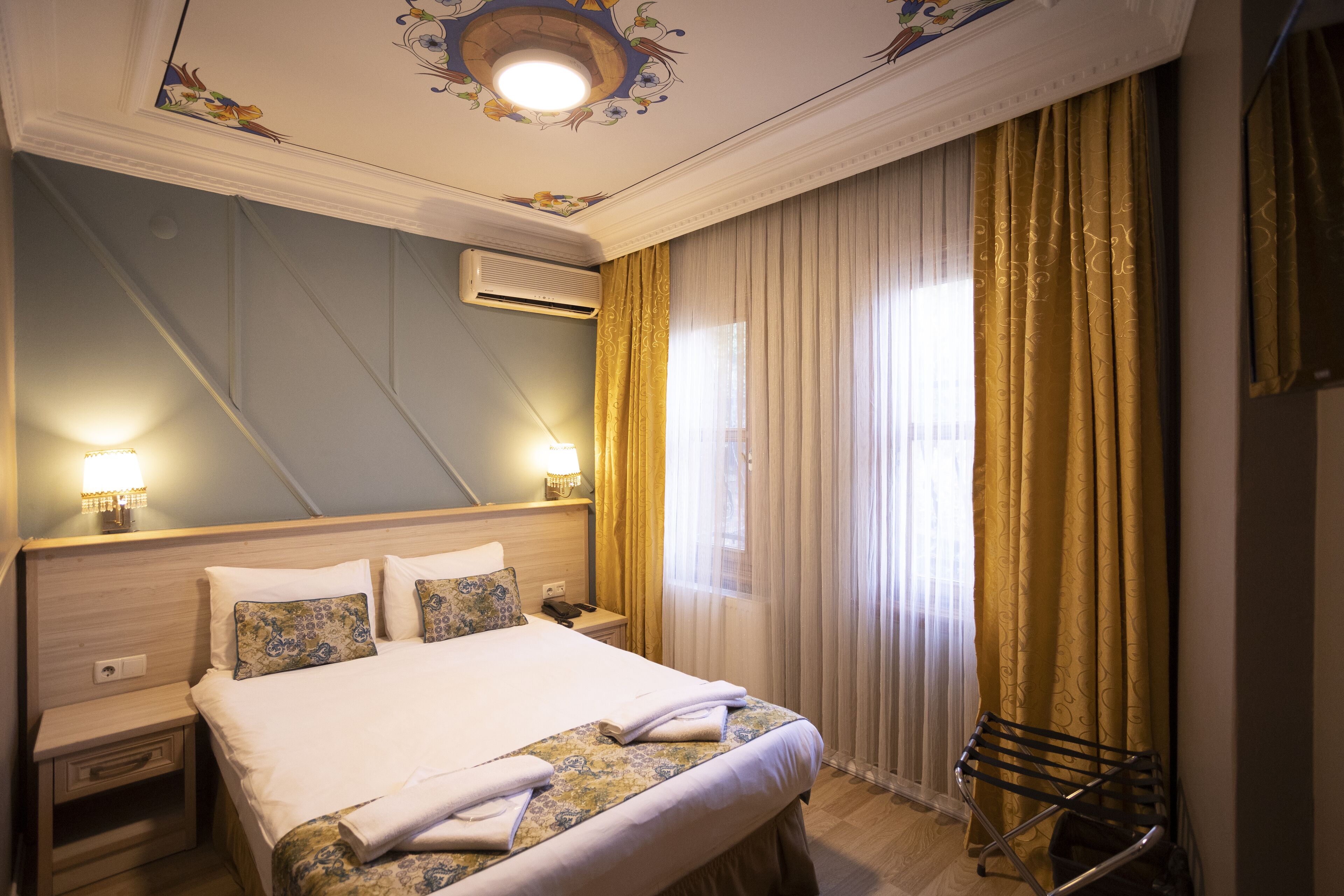 Ein Hotelzimmer mit einem großen Bett, einem Nachttisch, einer Klimaanlage, einer Lampe und einem Fenster mit Vorhängen.