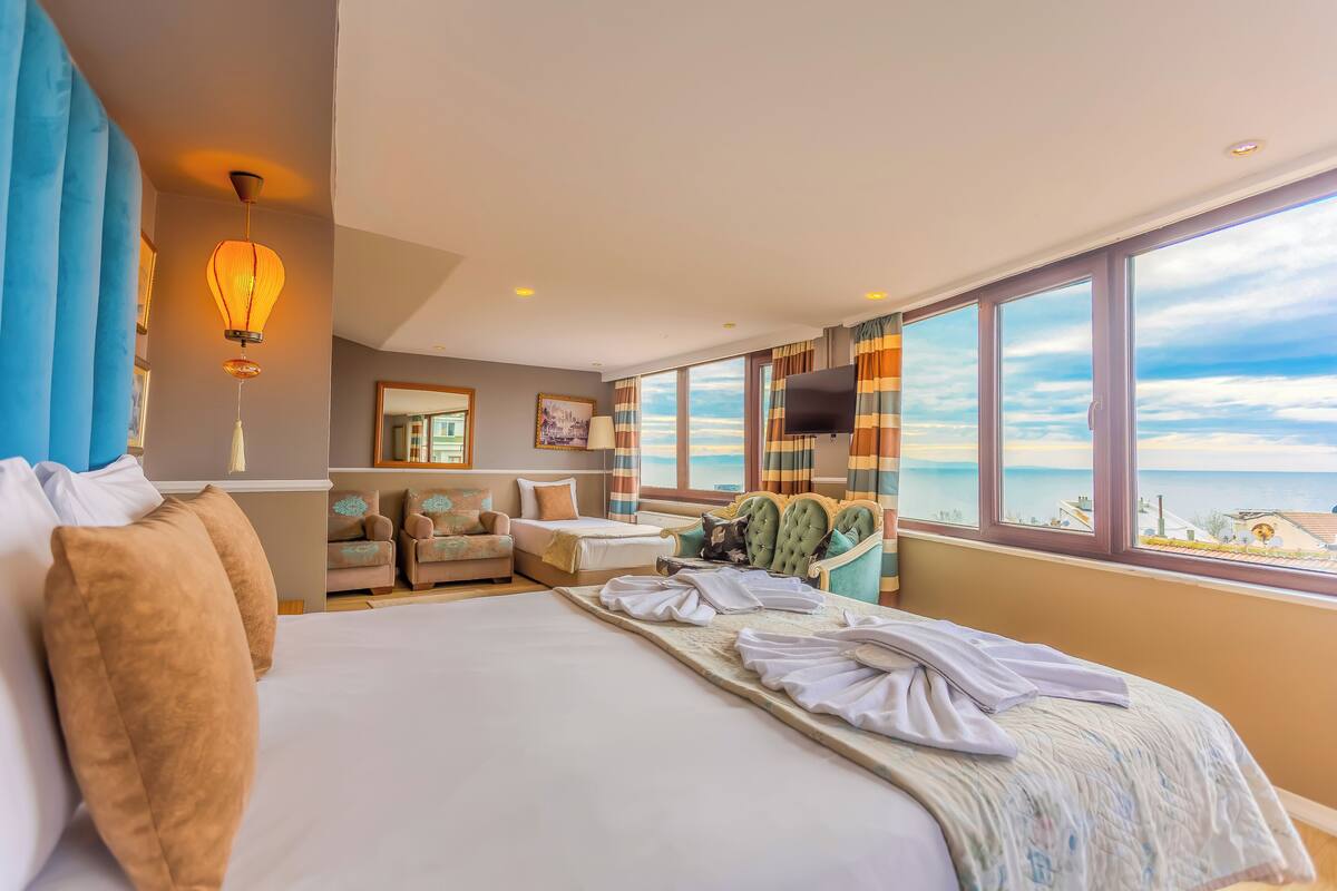 A hotel room with a large bed, a TV, a view of the sea, and a window with curtains.