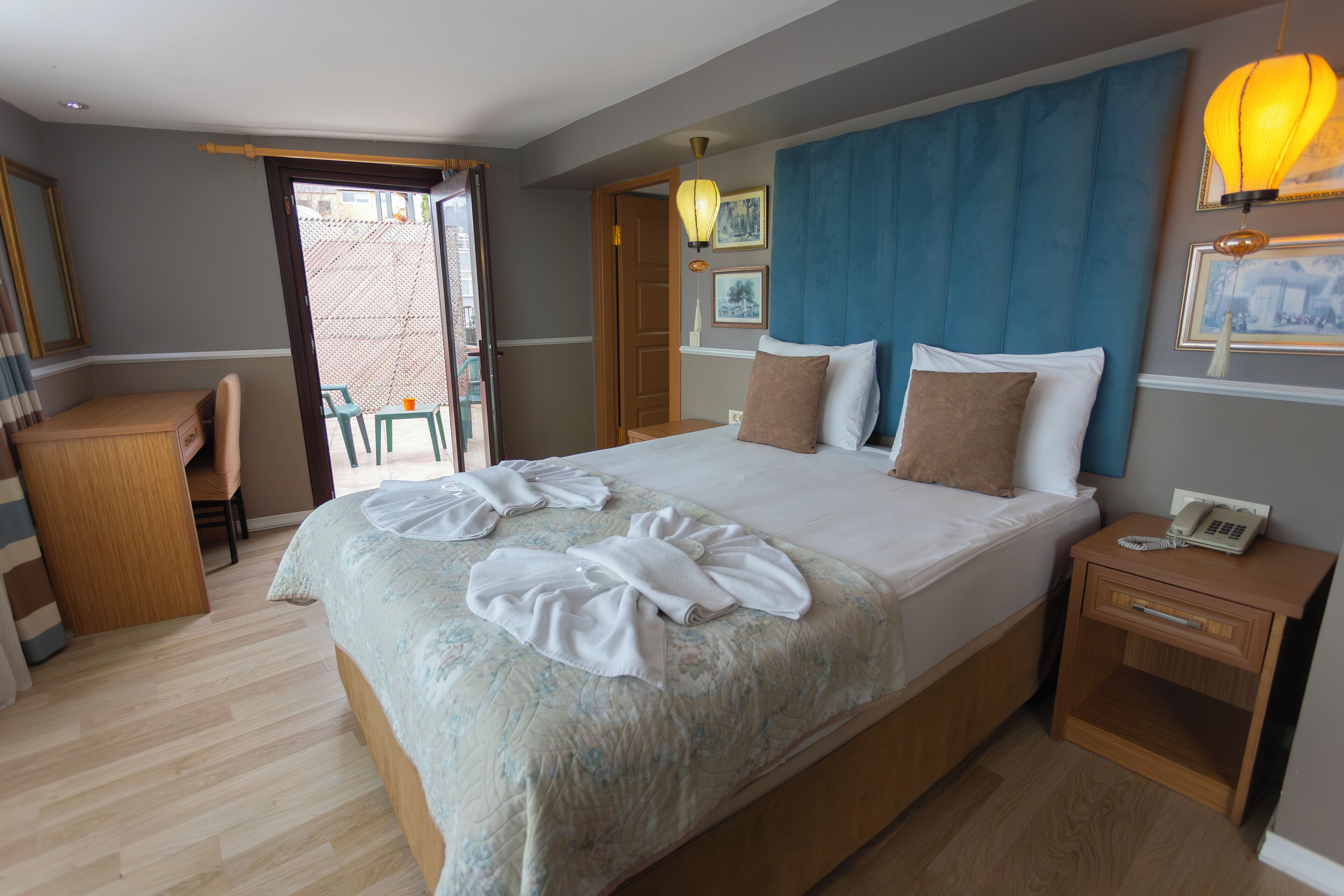 A neatly made bed with towels, a wooden nightstand with a phone, and a desk with a chair.