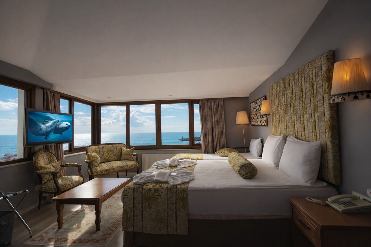 A hotel room with a large bed, a sofa, a TV, and a view of the sea.